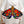 A person in a white blazer holds a stained-glass-style moth ornament with large red poppy flowers on black wings and iridescent rainbow accents near the base.